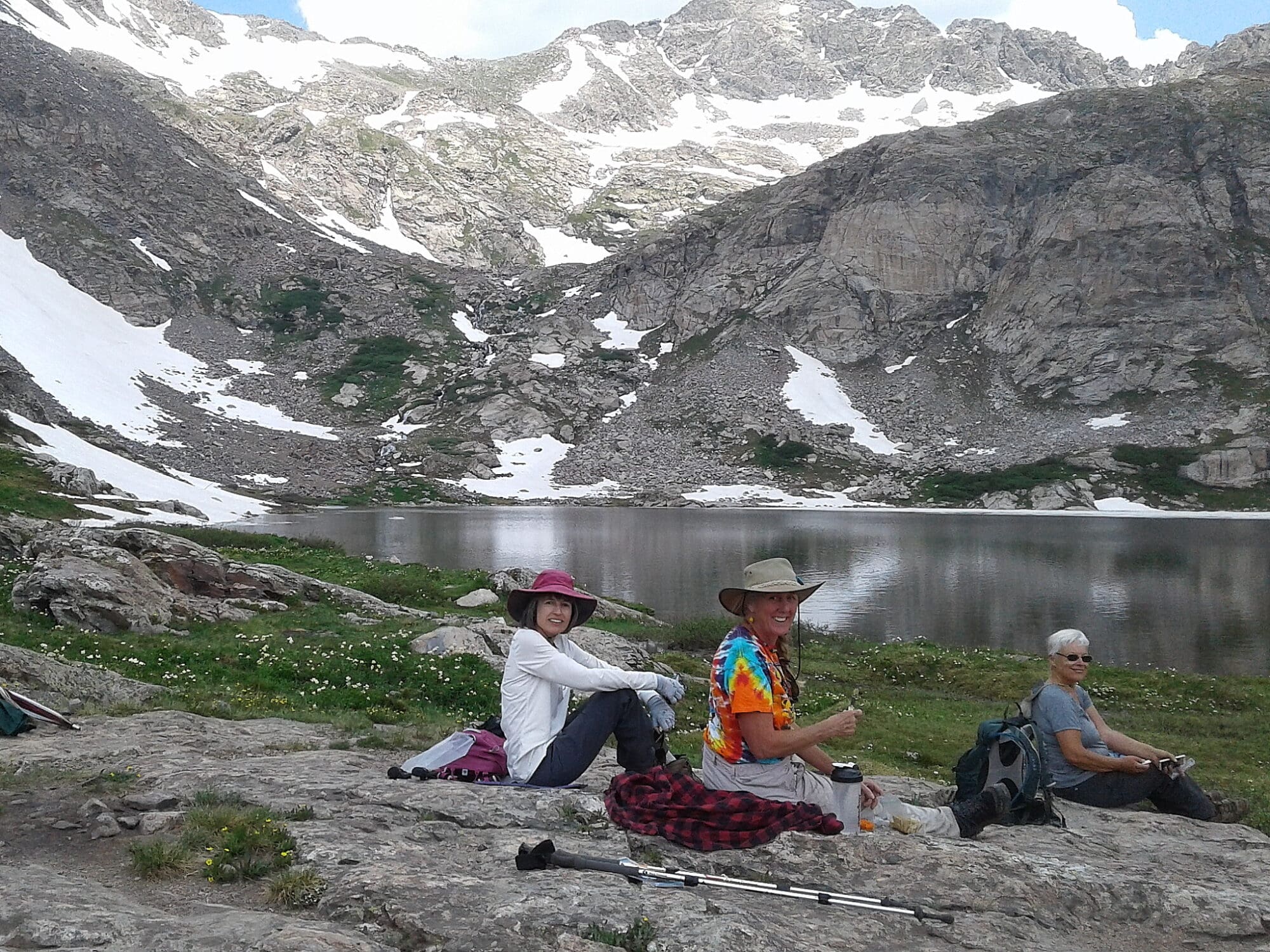 Garna Clubs - Hiking Club - Women sitting alongside high alpine lake with spots of snow on the mountainside