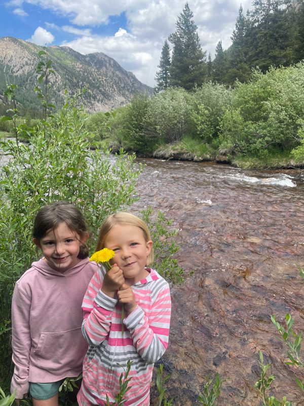 Two youth holding a dandelion for the camera alongside the river