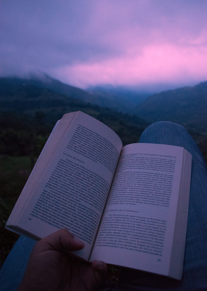 Book open on person's lap with the mountains in the backdrop